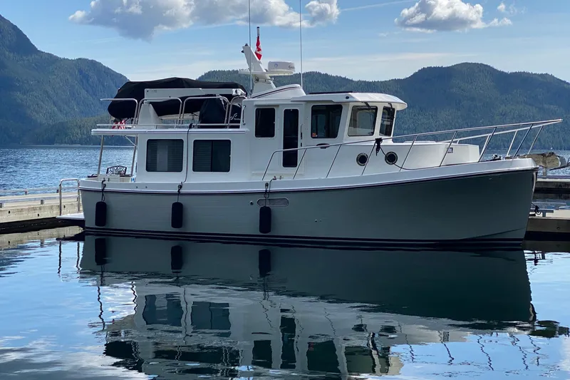 The Image of 2021 American Tug 362 docked on serene lake with mountainous backdrop. - 0
