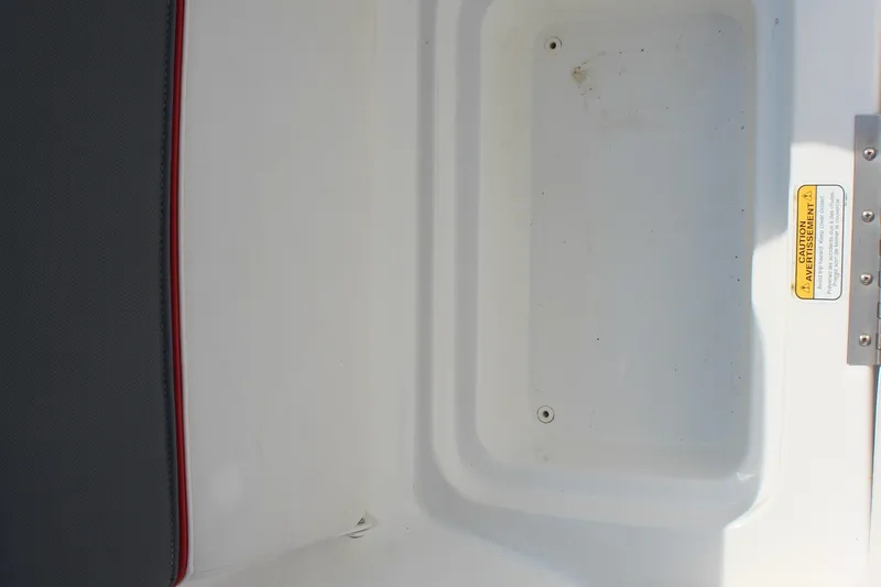 Slide: The Image of 2023 Tahoe T16 boat storage compartment with caution label and black-red seat edge. - 14