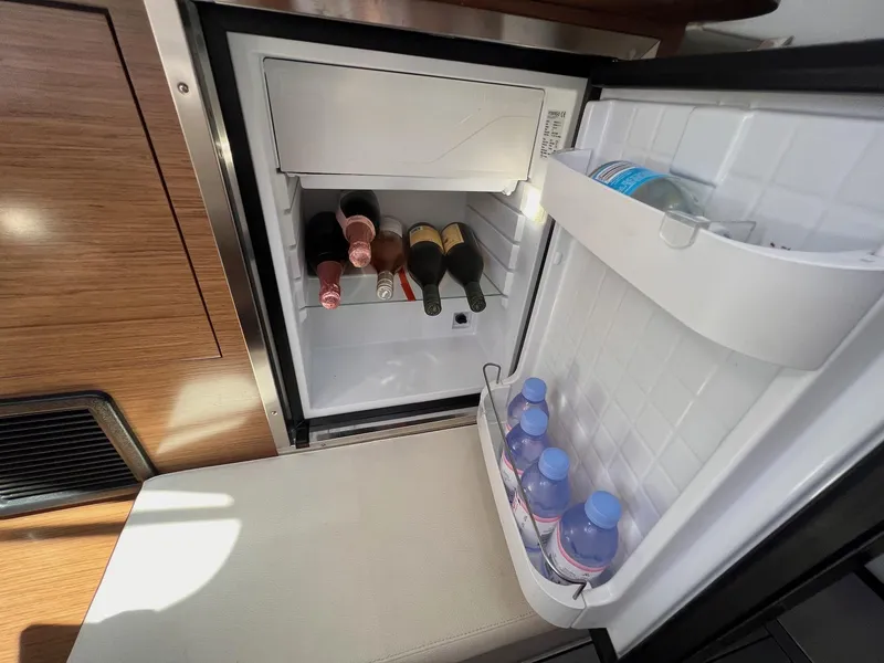 Slide: The Image of Open mini fridge on 2019 Cruisers Yachts 338 IO, stocked with beverages and wine bottles. - 29