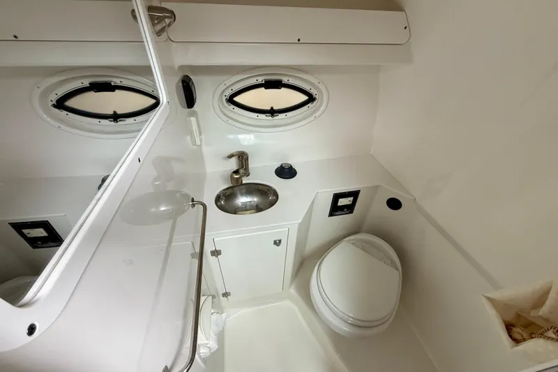 Slide: The Image of 2019 Monterey 295 Sport Yacht bathroom with sink, toilet, and porthole windows. - 18