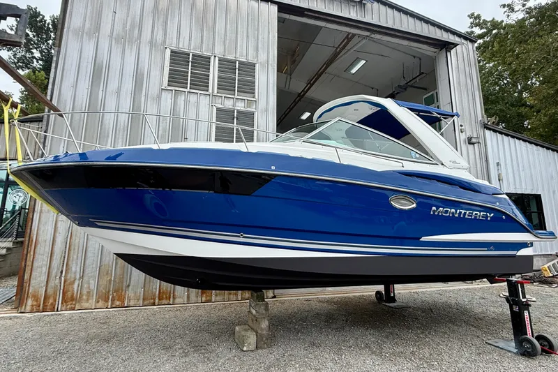 Slide: The Image of 2019 Monterey 295 Sport Yacht in blue, displayed outside a metal building. - 2
