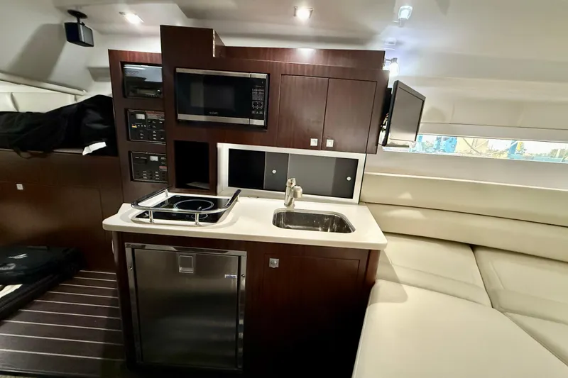 Slide: The Image of 2019 Monterey 295 Sport Yacht interior with kitchenette, featuring stove, sink, microwave, and seating area. - 20
