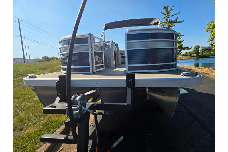 Slide: The Image of 2022 Bennington L 22 L-Bench pontoon boat on trailer, parked near a lake. - 6