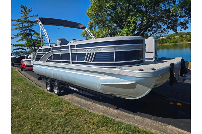 Slide: The Image of 2022 Bennington L 22 L-Bench pontoon boat on trailer by a lake. - 8