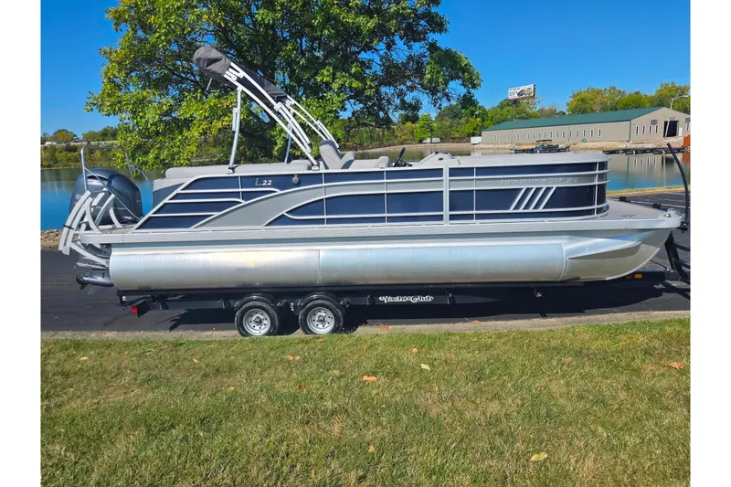 Slide: The Image of 2022 Bennington L 22 L-Bench pontoon boat on trailer by a lake. - 9