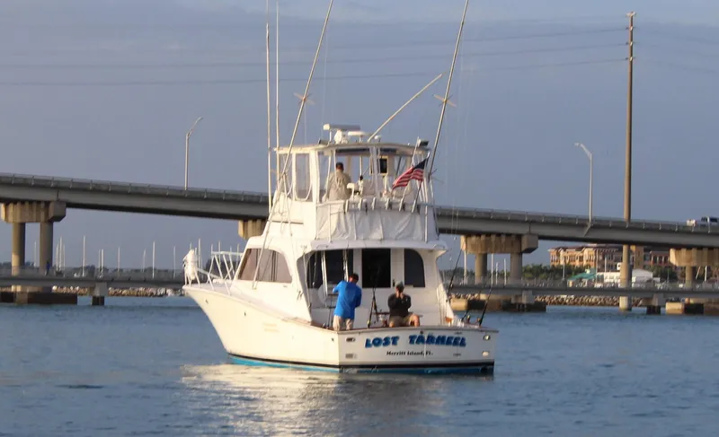 Slide: The Image of 1990 Post 44 Sport Fisherman boat on water near a bridge, with people on deck. - 2
