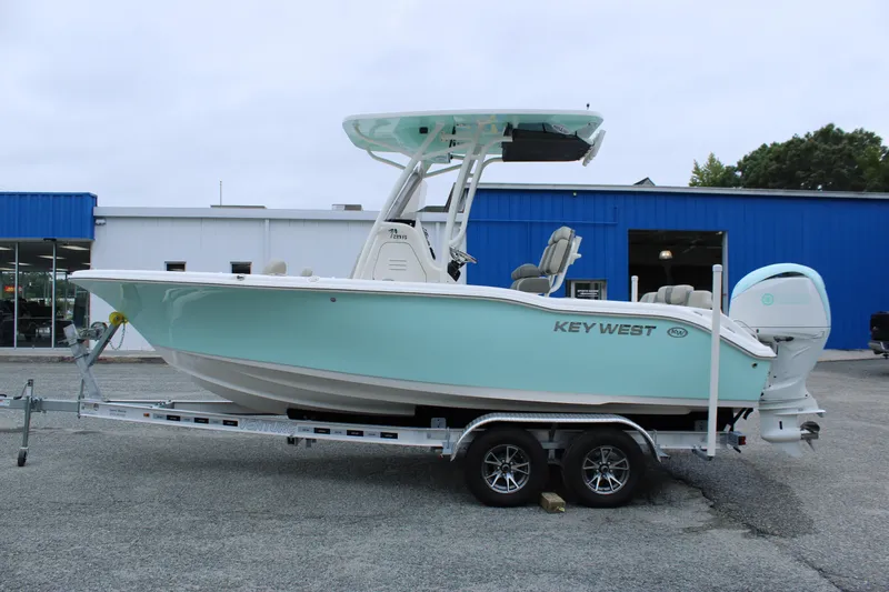 Slide: The Image of 2026 Key West 219 FS boat on trailer, light blue hull, parked outside a blue building. - 5