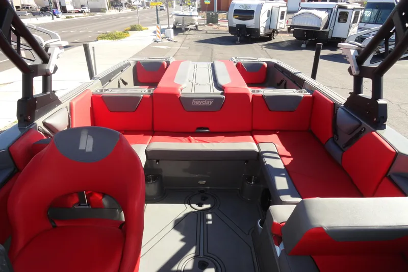 Slide: The Image of 2022 Heyday WT Surf boat interior with red and gray seating, parked near RVs. - 19