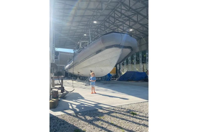 Slide: The Image of Child standing near a large 2004 Custom Pilot boat in a sunlit boatyard. - 76