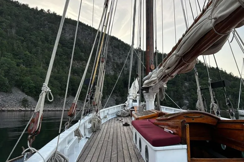 Slide: The Image of Deck view of 2004 Custom Luke Powell Pilot Cutter, surrounded by lush forested cliffs. - 16