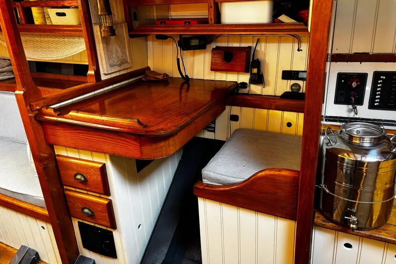 Slide: The Image of Cozy 2004 Luke Powell Pilot Cutter interior with wooden desk, seating, and nautical equipment. - 30