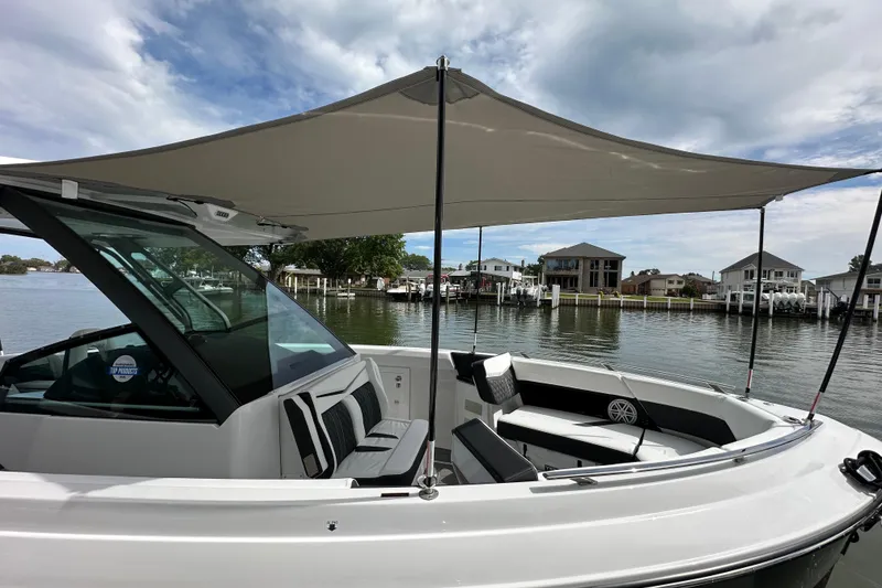 Slide: The Image of 2026 Monterey Elite 30 OB boat with canopy, docked by waterfront homes under cloudy sky. - 14