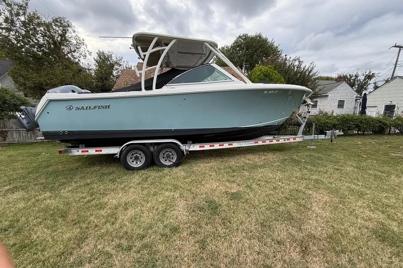 Slide: The Image of 2019 Sailfish 275 DC boat on trailer, parked on grass, cloudy sky background. - 4