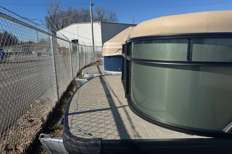 Slide: The Image of 2026 Godfrey Xperience 2286 SBX pontoon boat parked near a chain-link fence. - 11