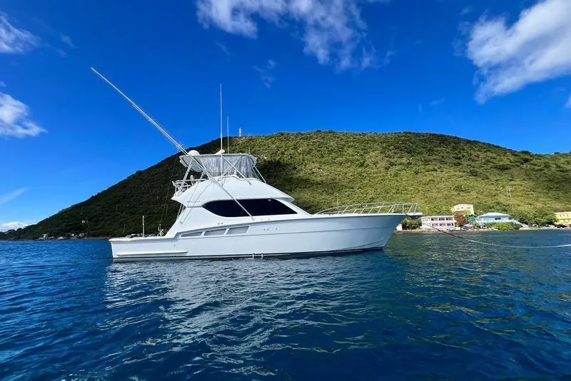 Slide: The Image of 2005 Hatteras 50 Convertible yacht anchored near lush green island under blue sky. - 5