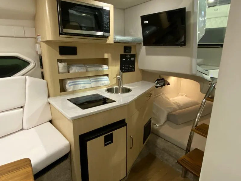 Slide: The Image of 2026 Regal 26 XO boat interior with kitchenette, microwave, TV, and cozy seating area. - 23