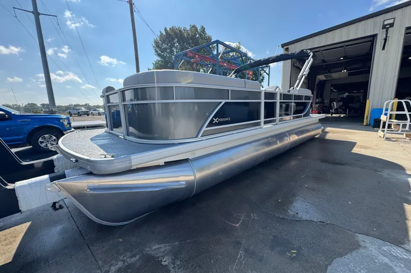 Slide: The Image of 2026 Sweetwater EX2286SBX pontoon boat parked outside a garage on a sunny day. - 1