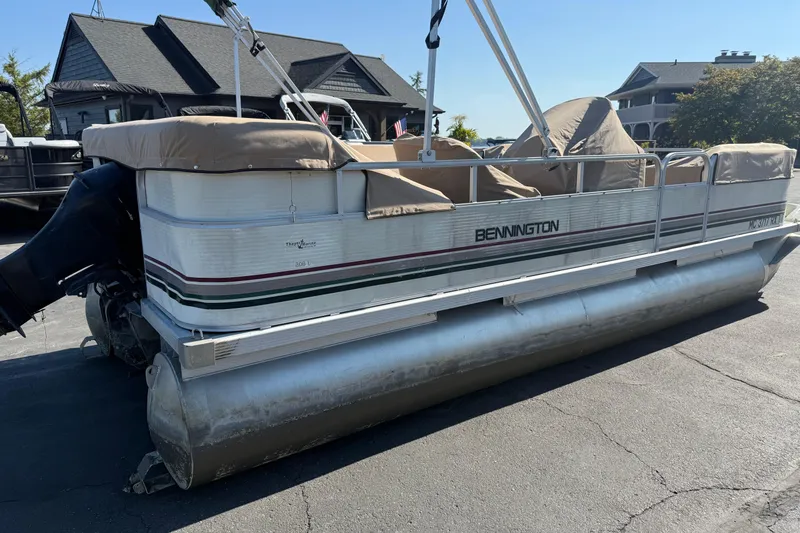 Slide: The Image of 1999 Bennington 208 L pontoon boat parked on pavement, covered seats, outboard motor visible. - 6