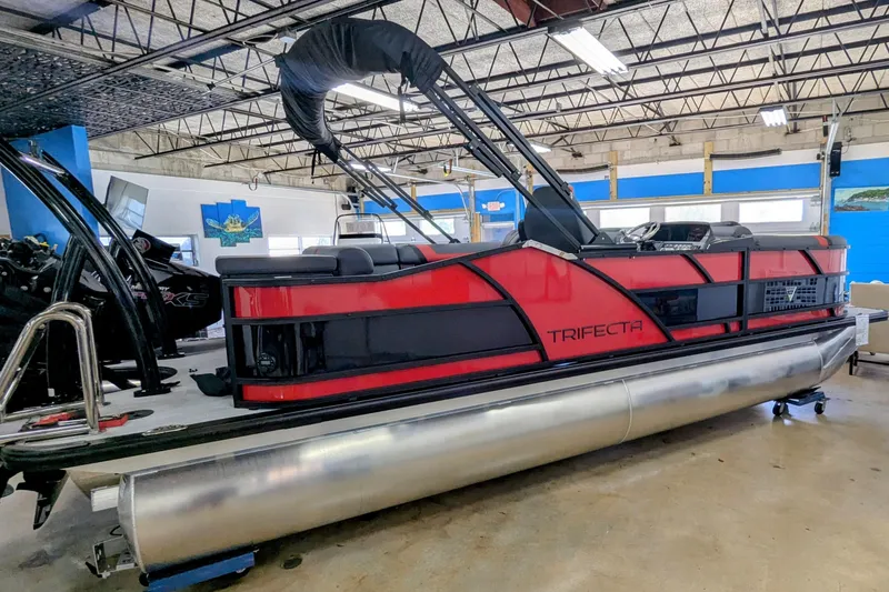 Slide: The Image of 2026 Trifecta 21C SS pontoon boat in showroom, featuring sleek red and black design. - 21