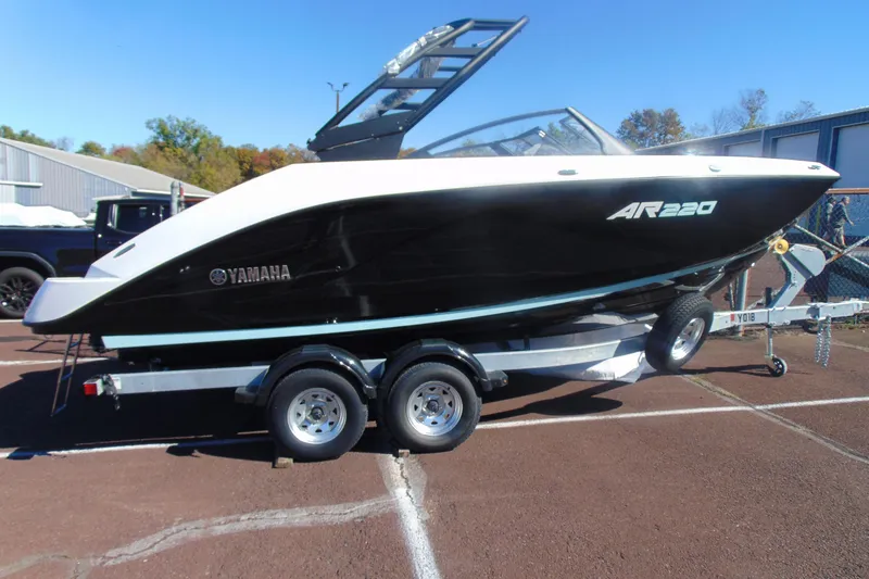 The Image of 2026 Yamaha Boats AR220 on trailer, black and white design, parked outdoors. - 1