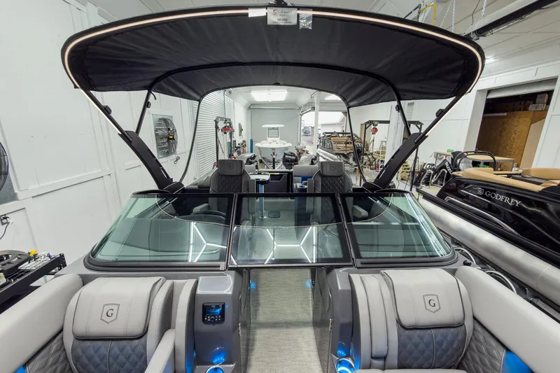 Slide: The Image of 2026 Godfrey Sanpan 27' Tritoon with split bench, windshield, and luxury seating in showroom. - 10