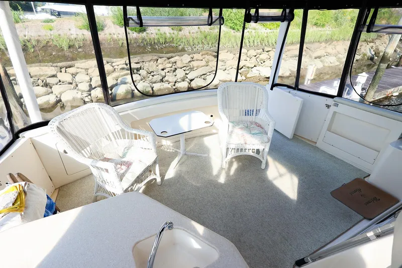 Slide: The Image of 2002 Silverton 43 Motor Yacht interior with wicker chairs and table, overlooking rocky shoreline. - 8