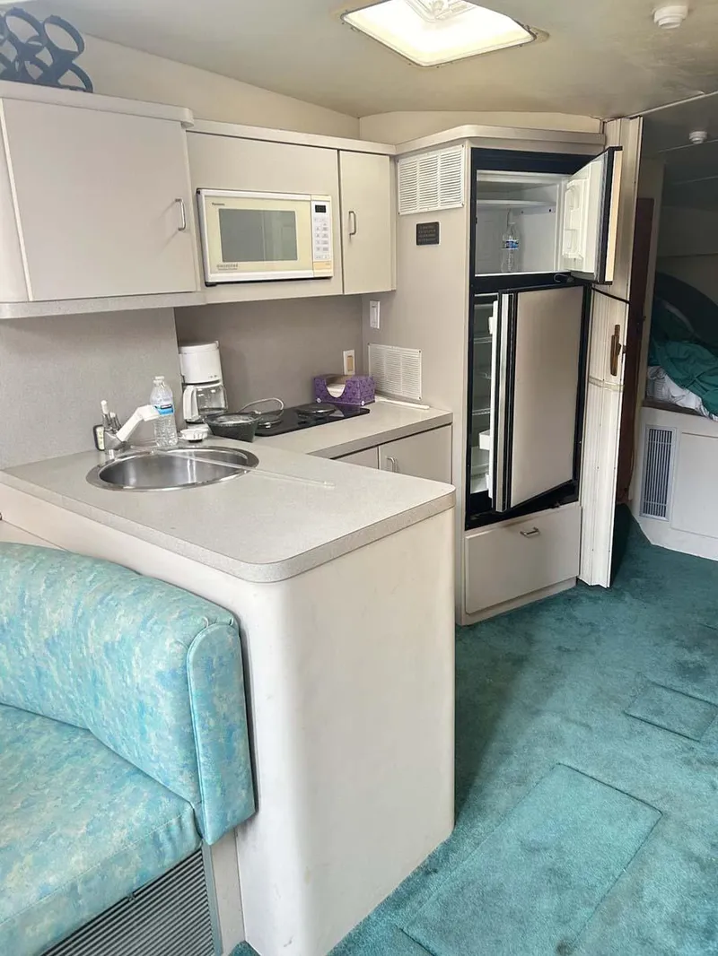 Slide: The Image of 1993 Mainship 36 Express interior with kitchenette, microwave, fridge, and teal carpet. - 6