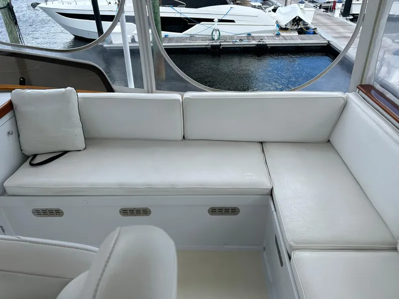 Slide: The Image of 1987 Lyman-Morse Downeast Flybridge interior with white seating, docked boats visible outside. - 32