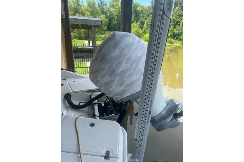 Slide: The Image of 2024 Boston Whaler 250 Dauntless boat engine with camouflage cover, docked by a river. - 2