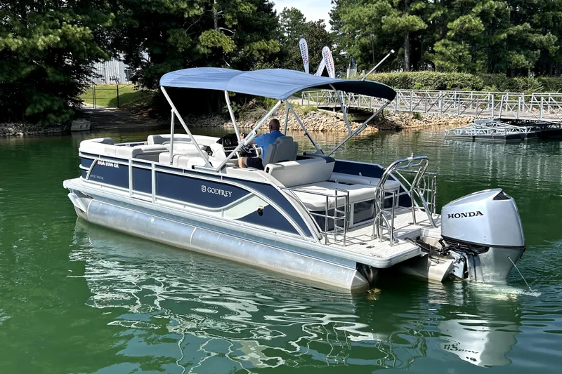 Slide: The Image of 2025 Godfrey SWEETWATER 2286 SFL pontoon boat on a serene lake with Honda outboard. - 2