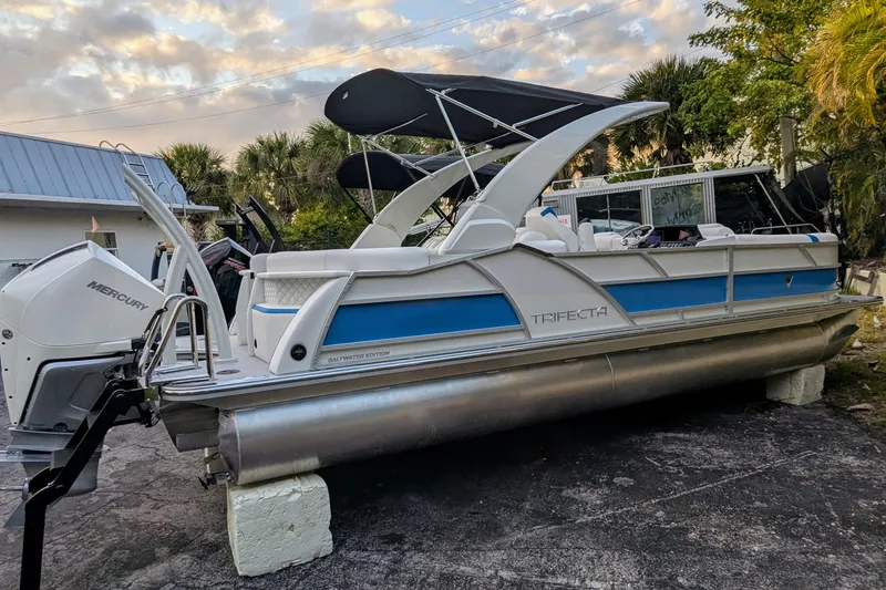 Slide: The Image of 2026 Trifecta 25 RF SS Arch pontoon boat with Mercury engine, parked outdoors. - 20