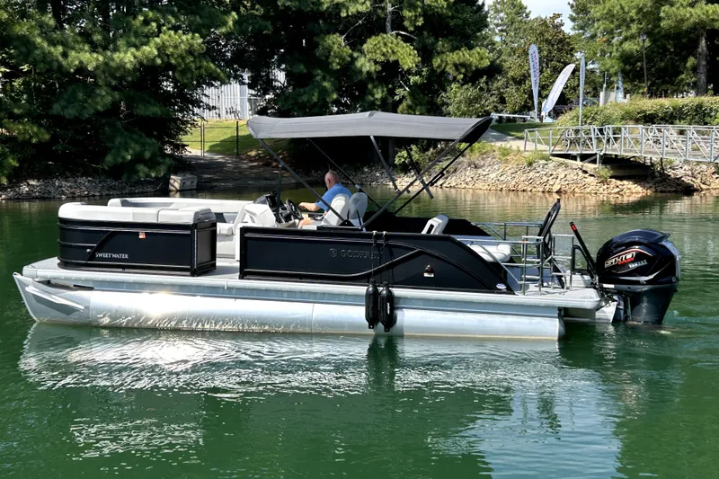 Slide: The Image of 2026 Godfrey Sweetwater 2486 SFLC pontoon boat on a serene lake with lush greenery. - 0