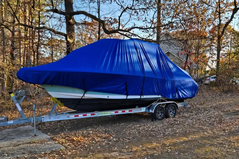 Slide: The Image of 2023 Sea Hunt Ultra 265 SE boat covered with blue tarp on trailer in wooded area. - 20