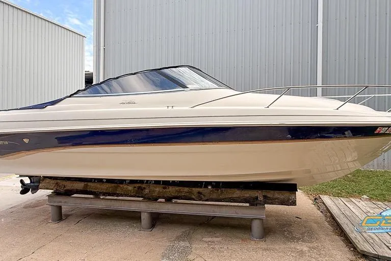 Slide: The Image of 1998 Monterey 236 Montura boat on display, white and blue hull, parked outdoors. - 24