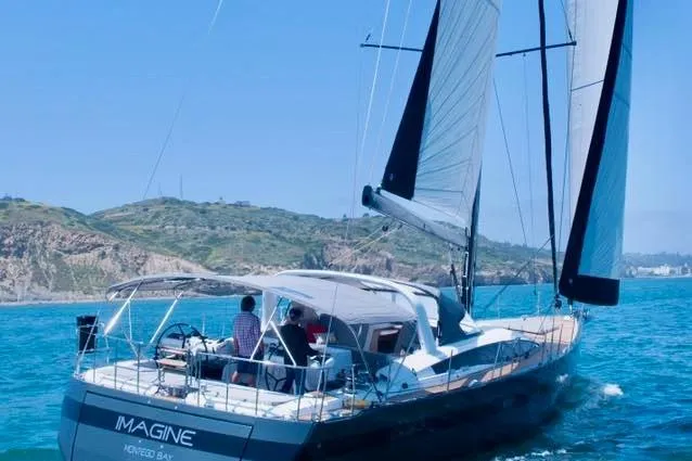 Slide: The Image of 2017 Jeanneau 64 sailboat "Imagine" cruising near a scenic coastline. - 2