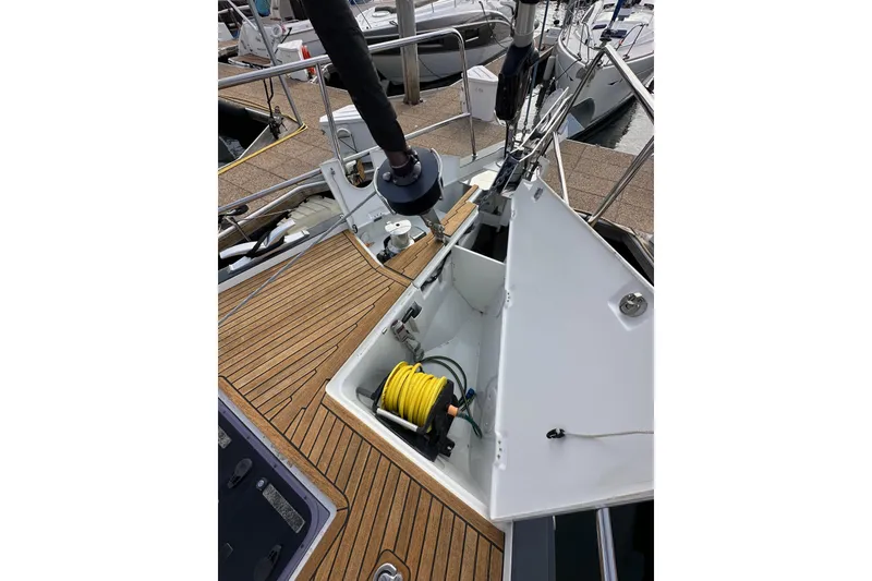 Slide: The Image of 2017 Jeanneau 64 sailboat deck with open storage compartment and coiled yellow hose. - 23