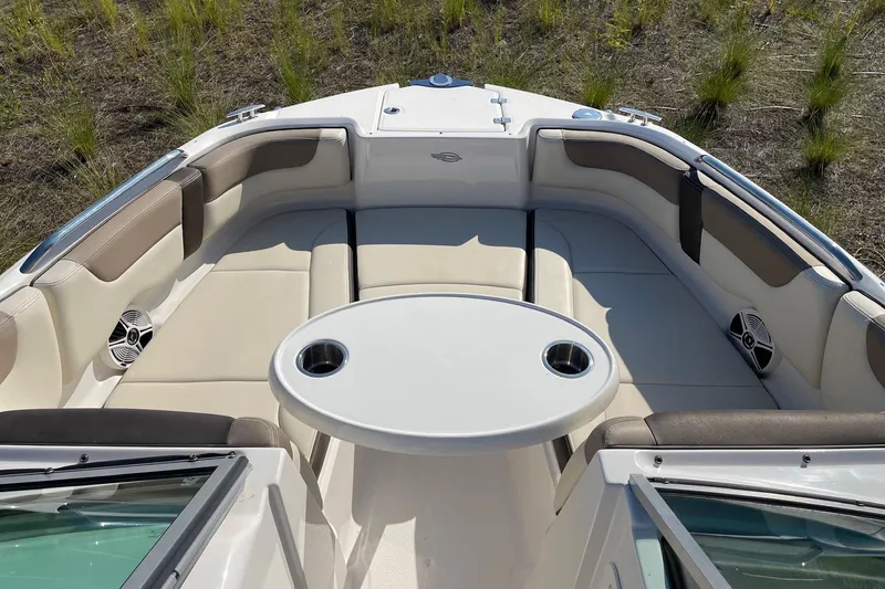 Slide: The Image of 2019 Chaparral 210 Suncoast boat interior with seating and table, surrounded by grass. - 28