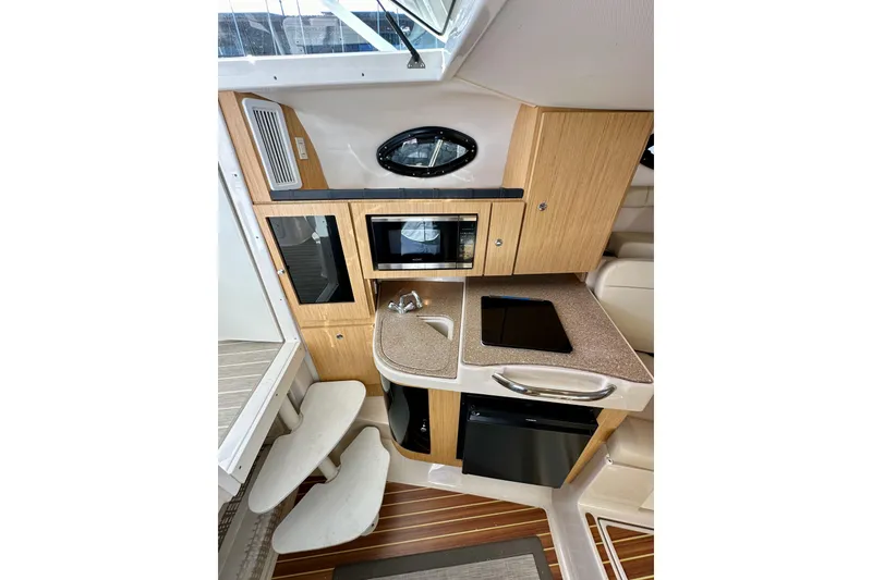 Slide: The Image of 2018 Wellcraft 290 Coastal boat interior with kitchenette, featuring wood cabinetry and modern appliances. - 28