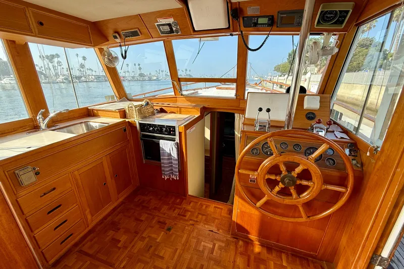 Slide: The Image of 1982 Grand Banks 42 Motoryacht interior with wooden helm, kitchen, and waterfront view. - 10