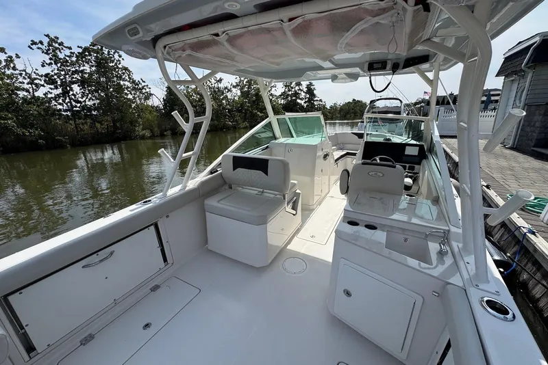 Slide: The Image of 2022 Sailfish 276 DC boat interior with seating and helm, docked by a calm river. - 9
