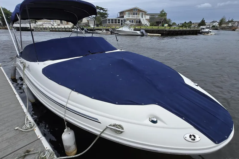 Slide: The Image of 2005 Sea Ray 220 Sundeck boat docked with blue cover, waterfront view. - 12