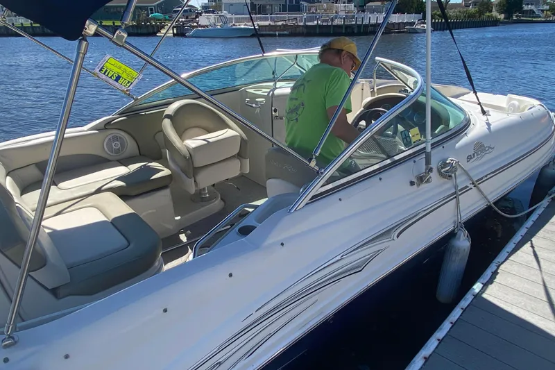 Slide: The Image of 2005 Sea Ray 220 Sundeck boat docked, featuring spacious seating and a person at the helm. - 20