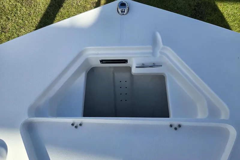 Slide: The Image of 2026 NauticStar 191 Hybrid boat storage compartment, open and empty, on grassy background. - 16