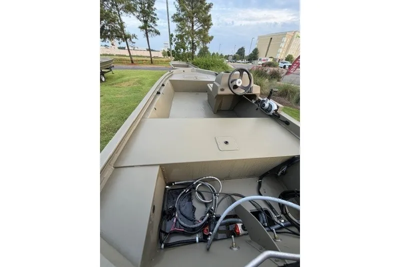 Slide: The Image of 2026 Tracker Grizzly 1648 SC boat interior with steering console, parked outdoors. - 8