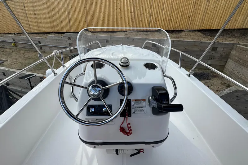 Slide: The Image of 2016 Edgewater 158CS boat console with steering wheel and controls, docked near wooden fence. - 11