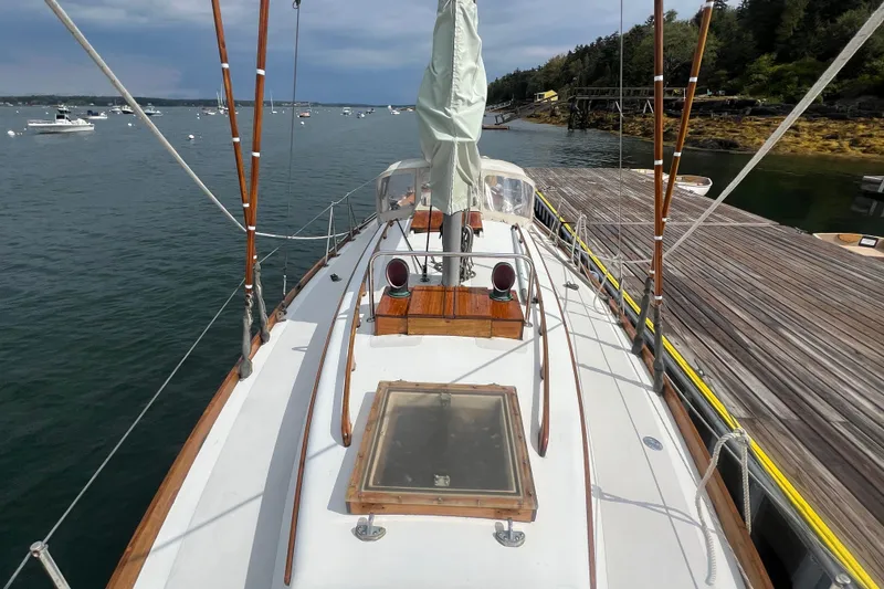 Slide: The Image of 1964 Hinckley Pilot 35 Sloop docked, showcasing deck and mast, surrounded by calm waters. - 17