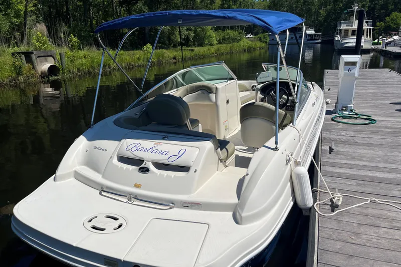 Slide: The Image of 2006 Sea Ray 200 Sundeck boat docked with blue canopy and lush greenery background. - 3
