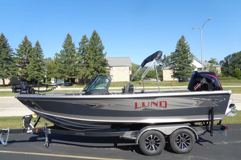 Slide: The Image of 2026 Lund 1975 Tyee boat on trailer, parked outdoors, with trees and houses in the background. - 2