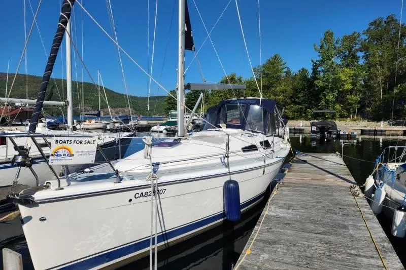 Slide: The Image of 2006 Hunter 33 sailboat docked, for sale, with clear blue sky and lush greenery. - 1