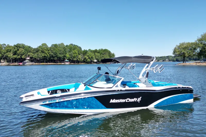 Slide: The Image of 2017 MasterCraft X26 boat on a serene lake with lush green trees. - 1